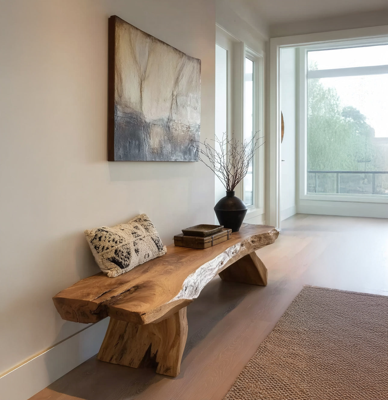 Natural wooden bench in minimalist hallway with decorative pillow, black vase with branches, and abstract painting